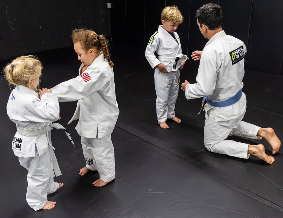 Young students paired up practicing grips while a coach kneels beside them in kids class