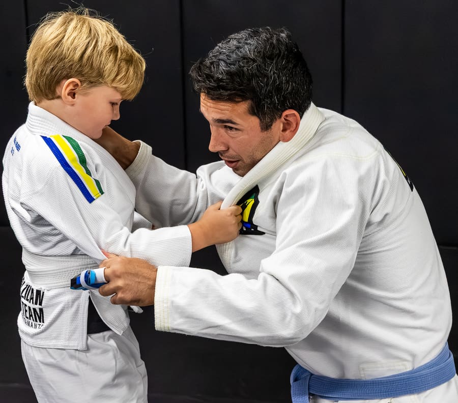 A coach teaching a young beginner how to grip the gi, one on one