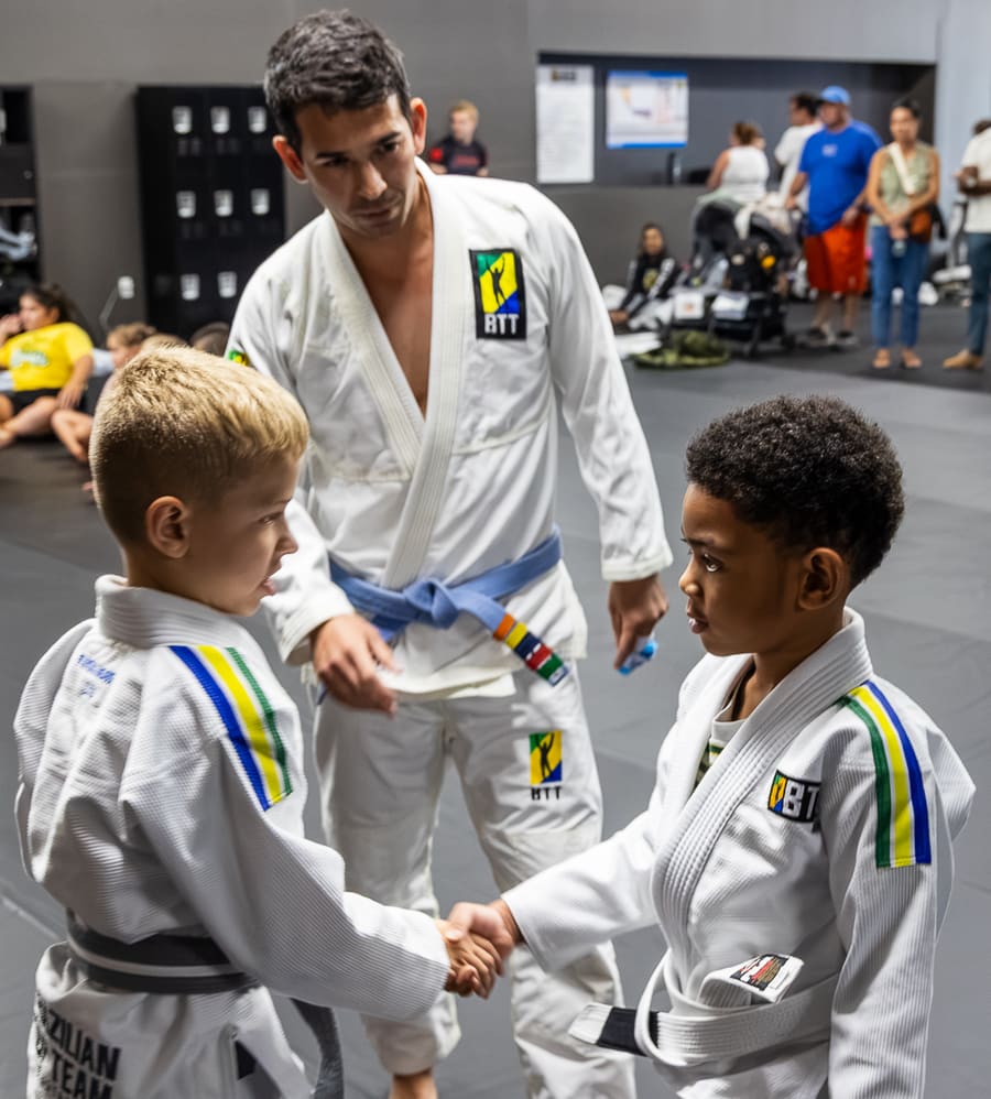 A coach guiding two young students through a technique in kids class
